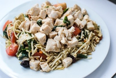 A plate of noodle salad with pieces of chicken on top.