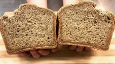 A pair of hands hold a loaf of brown bread which has been cut in half. 
