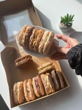 A hand holds a plate of pastries above a takeaway food box containing more pastries.